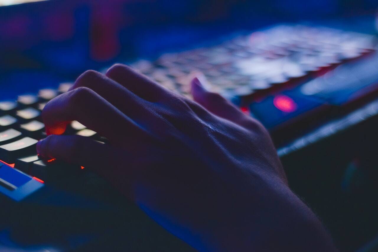 A hand resting on a backlit keyboard in a dimly lit room
